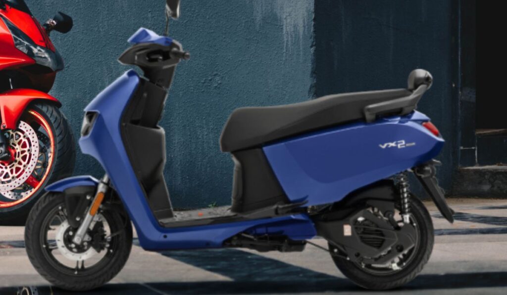 Create a featured image of Hero Vida VX2 electric scooter, in bright orange and white color, parked on a clean city street. Add icons of battery, mobile app, and 100km range. Show headline in top-left: ‘Hero Vida VX2 is Here’. Clean, youth-focused, eco-style layout. Avoid generic e-scooters — match actual VX2 model look.